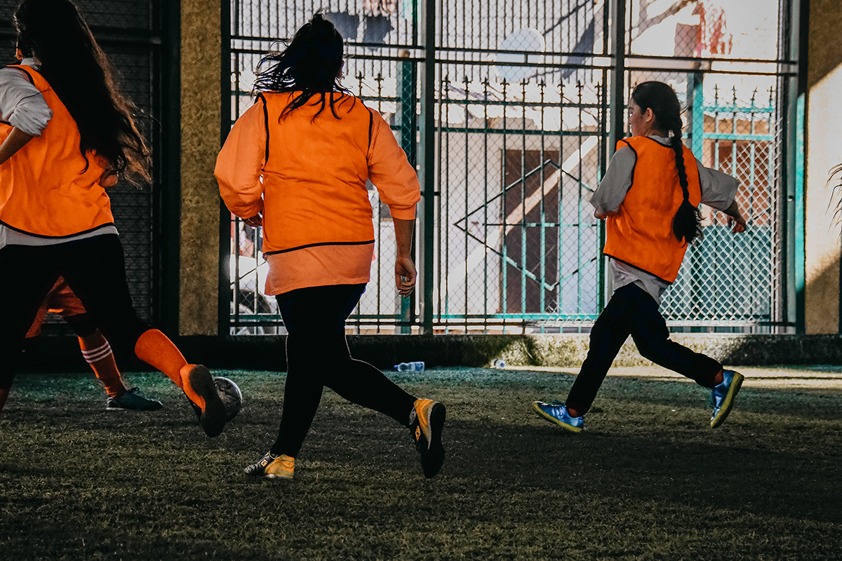 Refugee girls playing football in orange hi-vis vests