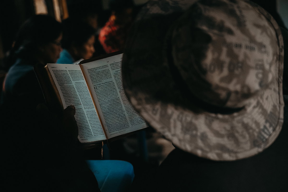 Person in a wide brim hat reading their Bible